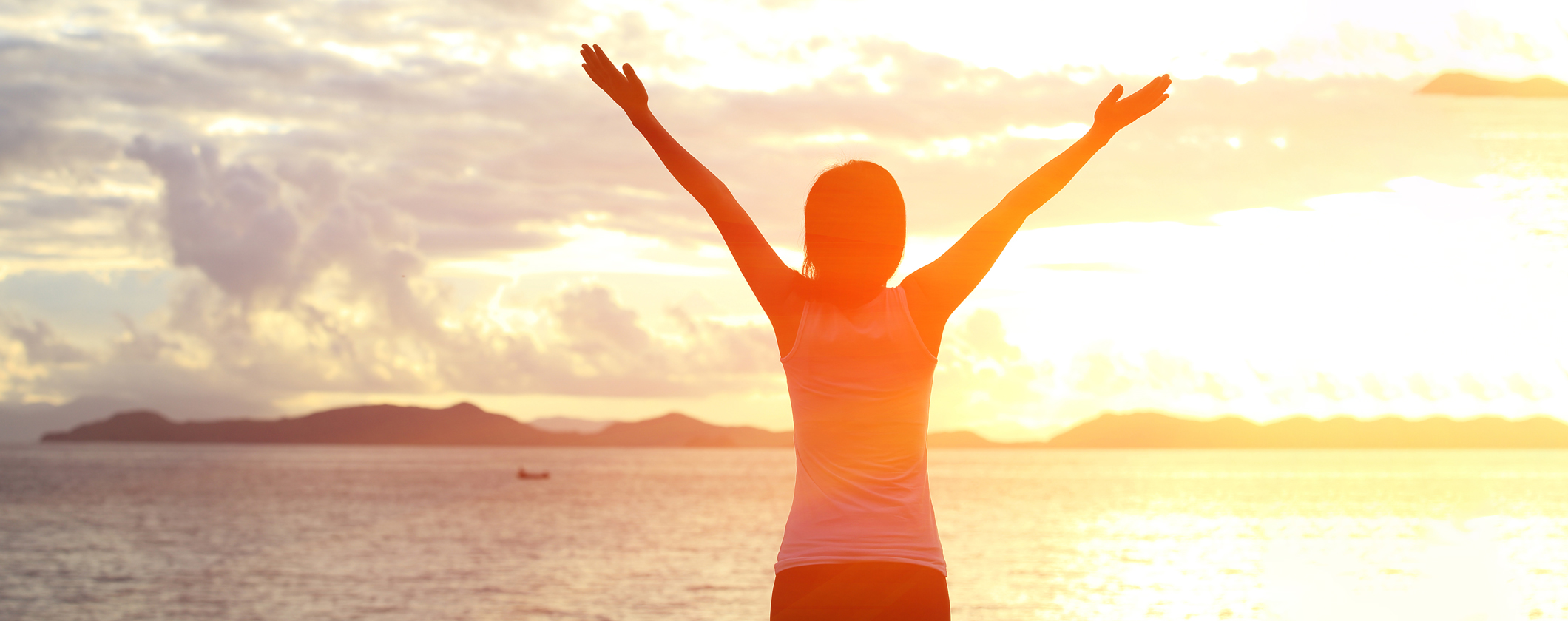 Person løfter armene og ser mot havet